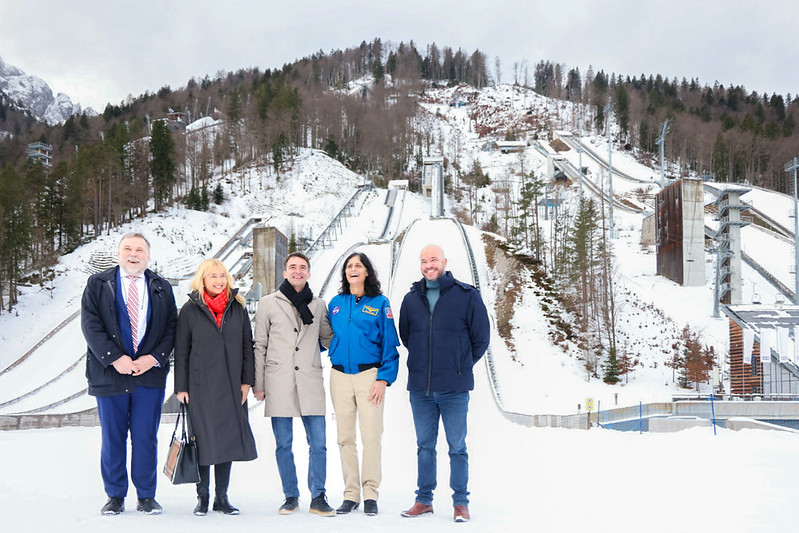 Dve ženski in trije moški stojijo eden zraven drugega. Zadaj se vidijo zasnežene skakalnice.