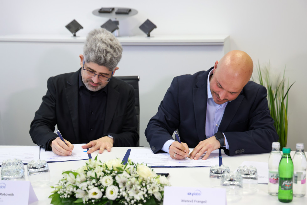 Moška sedita za mizo in podpisujeta pogodbo.