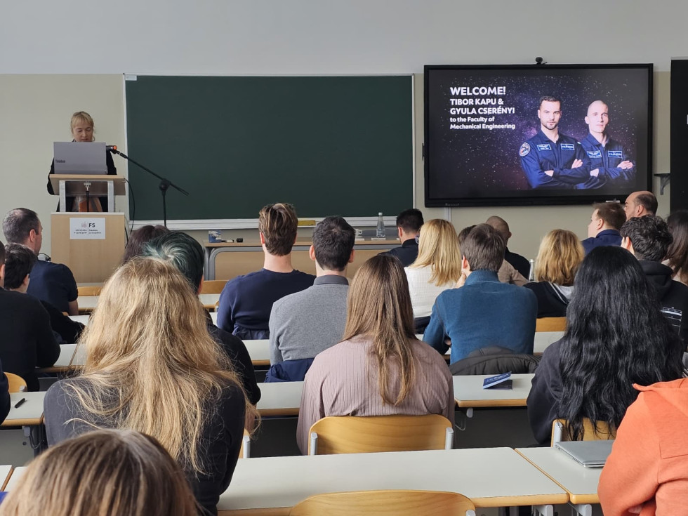 Udeleženci sedijo v predavalnici in poslušajo predstavitev na zaslonu.