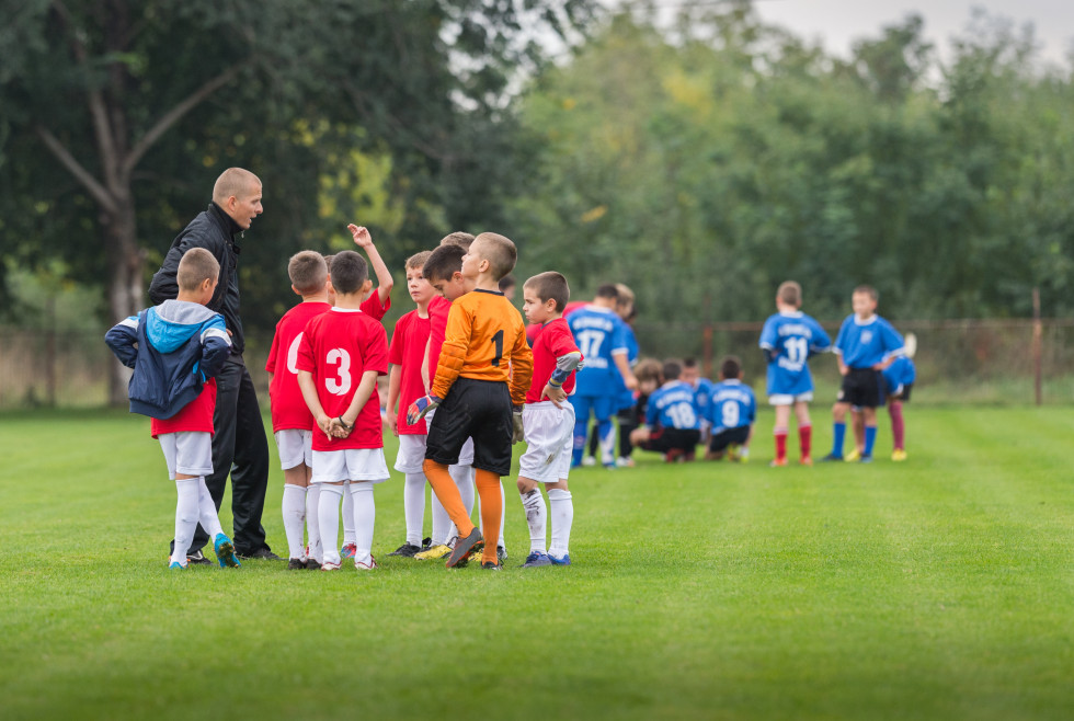 otroci v nogometni opravi so zbrani okoli trenerja