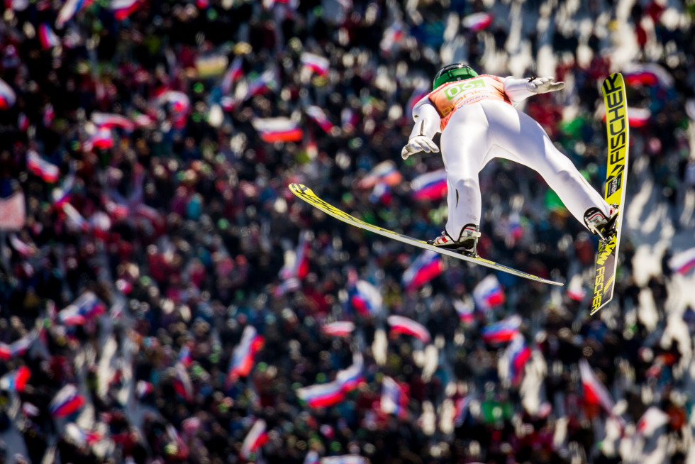 ski jumper from the back in the air and a crowd with Slovenian flags belove