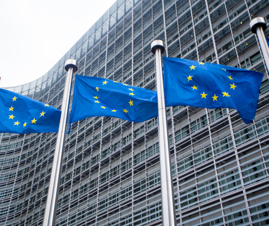 Tri zastave EU pred visoko stekleno-kovinsko zgradbo