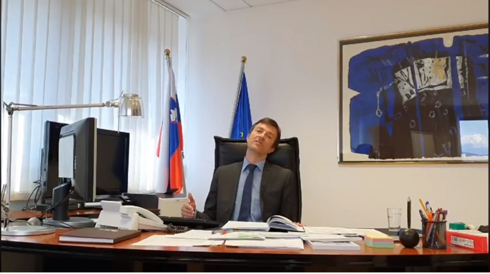  Državni sekretar Jure Gašparič sedi za svojo pisalno mizo v pisarni in govori proti kameri.