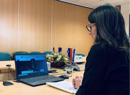 Slika ministrice s hrbtne strani, ki gleda v računalnik, kjer poteka videokonferenca.