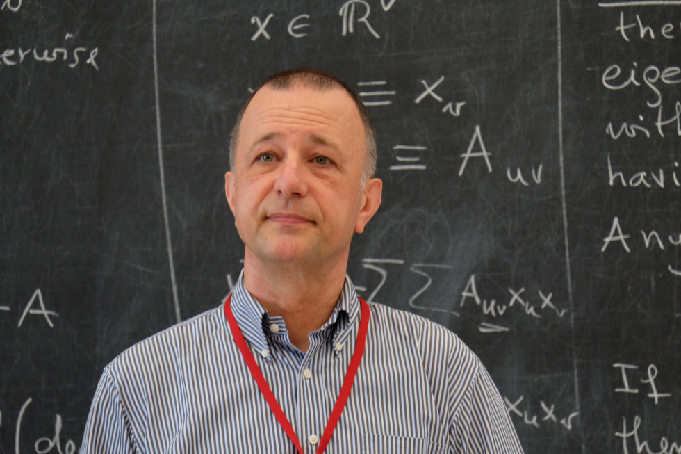 Portretna fotografija dr. Bojana Moharju pred tablo z matematičnimi formulami.