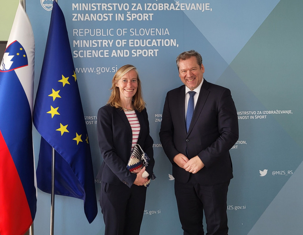Veleposlanica Sadler in minister Papič pred srečanjem na Ministrstvu za izobraževanje, znanost in šport, v ozadju slovenska in evropska zastava.