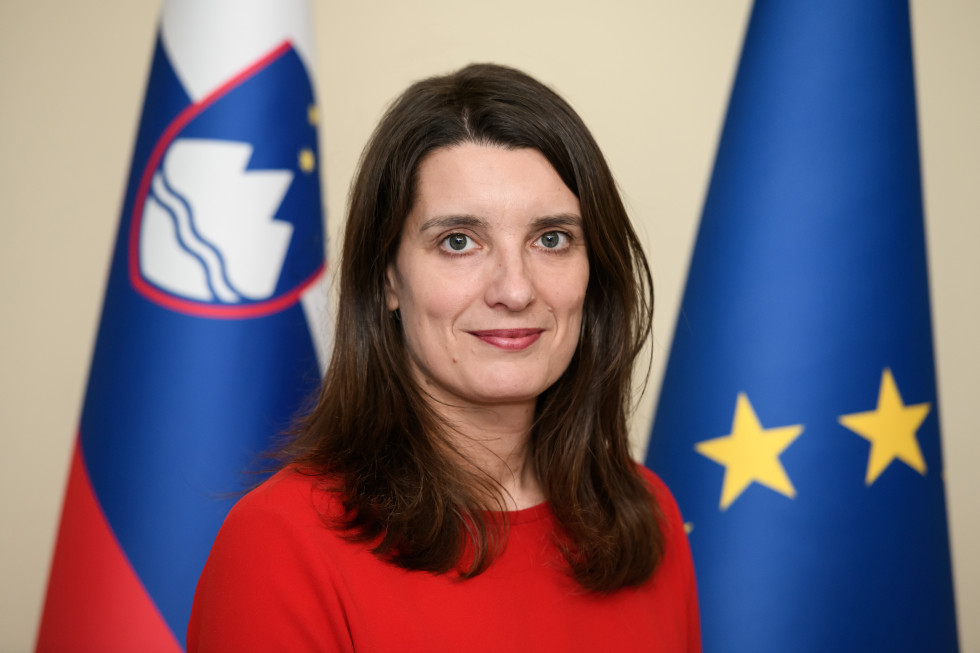 Avtoportret ministrice Kustec. V ozadju evropska in slovenska zastava.