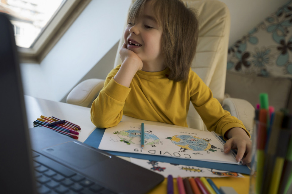  Deklica z risbo v naročju v svoji sobi za pisalno mizo in smeje gleda v računalnik.