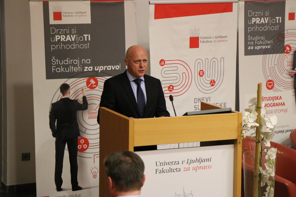 Minister Franc Props stoji za govornico, v ozadju je napis, ki promovira študij na Fakulteti za upravo 