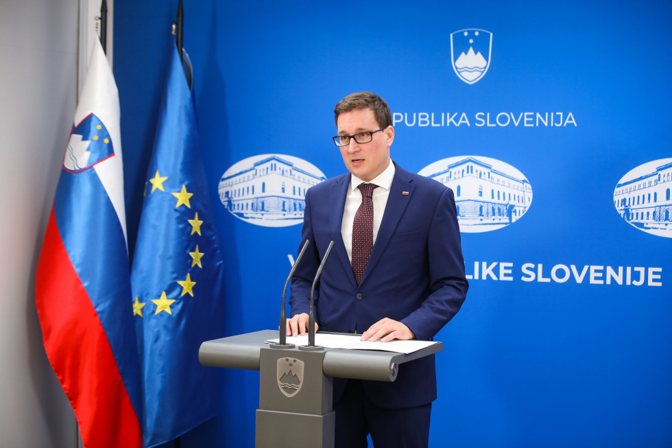 minister za govornico v vladnem tiskovnem središču, v ozadju slovenska in evropska zastava