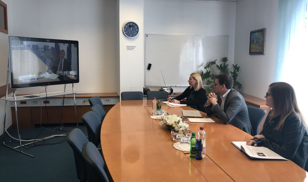 minister s sodelavci sedi za mizo pred zaslonom z video povezavo