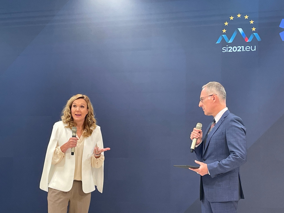 Petra Majdič in Igor Bergant stojita pred ozadjem, na katerem so logotipi konference in slovenskega predsedovanja, v rokah držita prenosna mikrofona