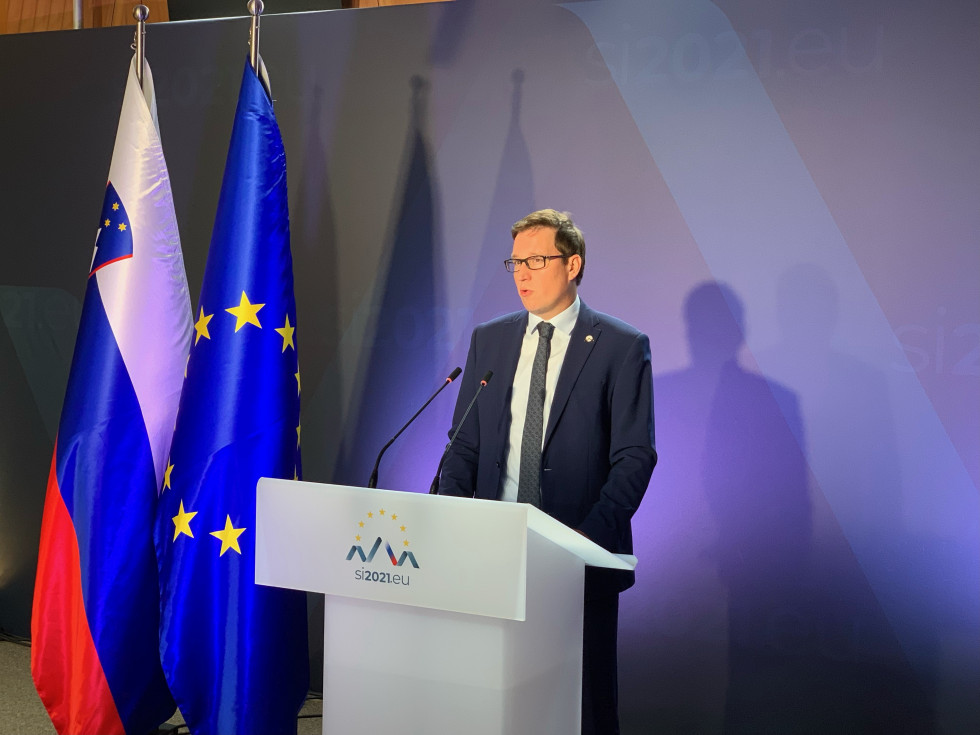 Minister pred govorniškim pultom, v ozadju slovenska in EU zastava.