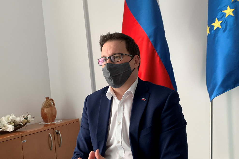 Minister pred ekranom računalnika nagovarja udeležence informativnega dne, v ozadju slovenska in EU zastava