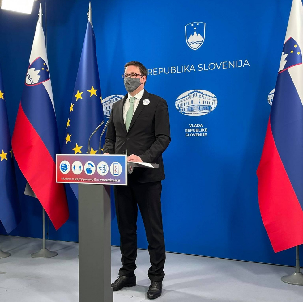 minister za govorniškim odrom daje izjavo, v ozadju slovenska za stava in zastava EU