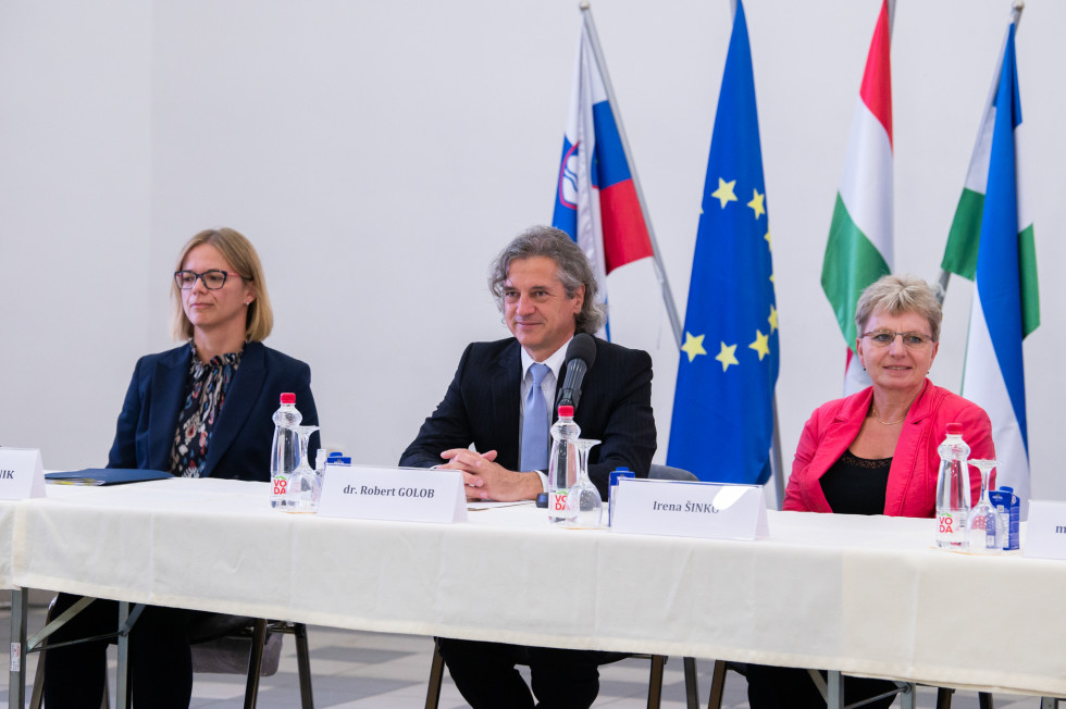 Predstavniki vlade sedijo za mizo v ozadju občinska, slovenska in EU zastava