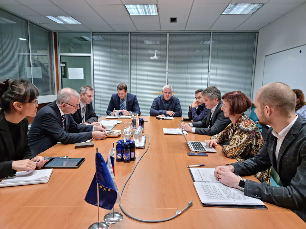 Sogovorniki sedijo v sejni sobi za ovalno mizo in diskutirajo. Na mizi tudi prenosni računalniki