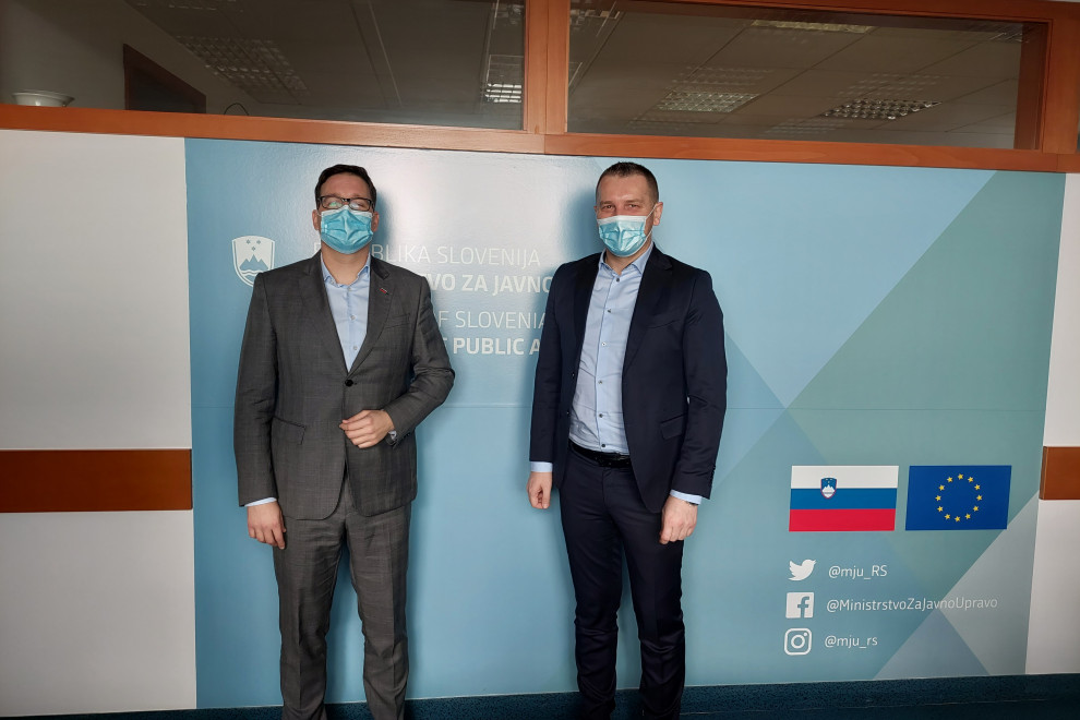 Skupinska fotografija, sogovornika stojita pred modrim panojem, na njem logotip ministrstva.