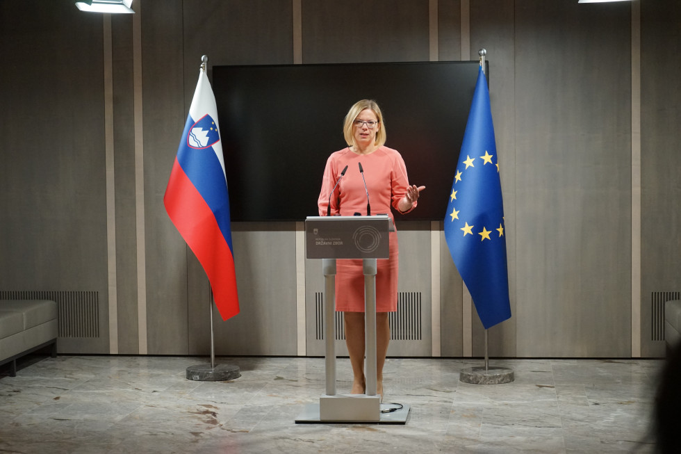 ministrica stoji za govornico, levo in desno od nje stojita slovenska in evropska zastava