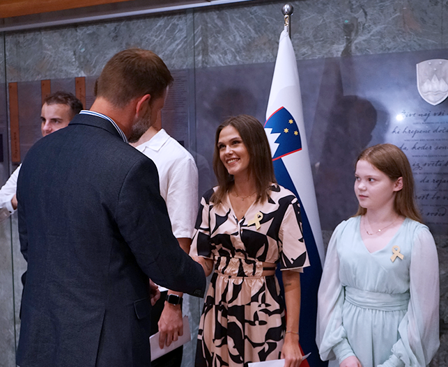 Trbič se rokuje z dekletom, za njima stoji slovenska zastava