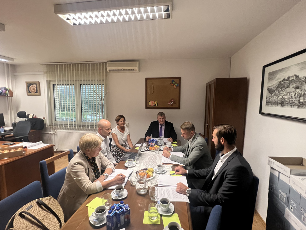 Za mizo sedijo načelniki in državni sekretar Trbič ter sodelavci, v ozadju okno in omara, na mizi sokovi, voda, kava