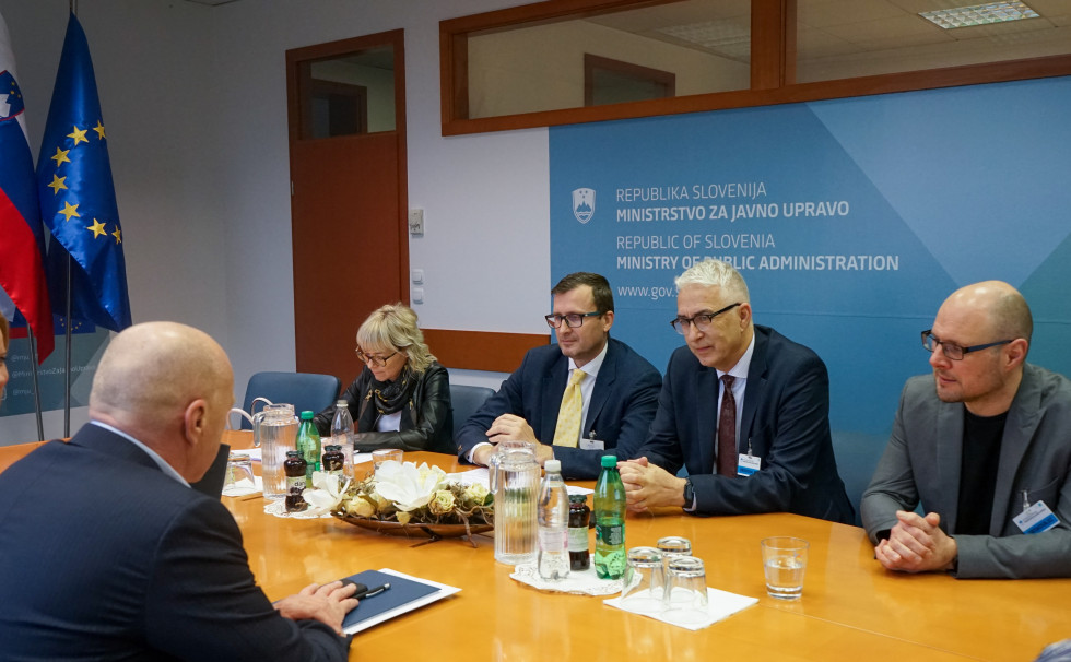 Minister in predstavniki GZS sedijo za mizo v sejni sobi, v ozadju logotip Ministrstva za javno upravo, vidita se tudi Slovenska zastava (desno) in Evropska zastava (levo)