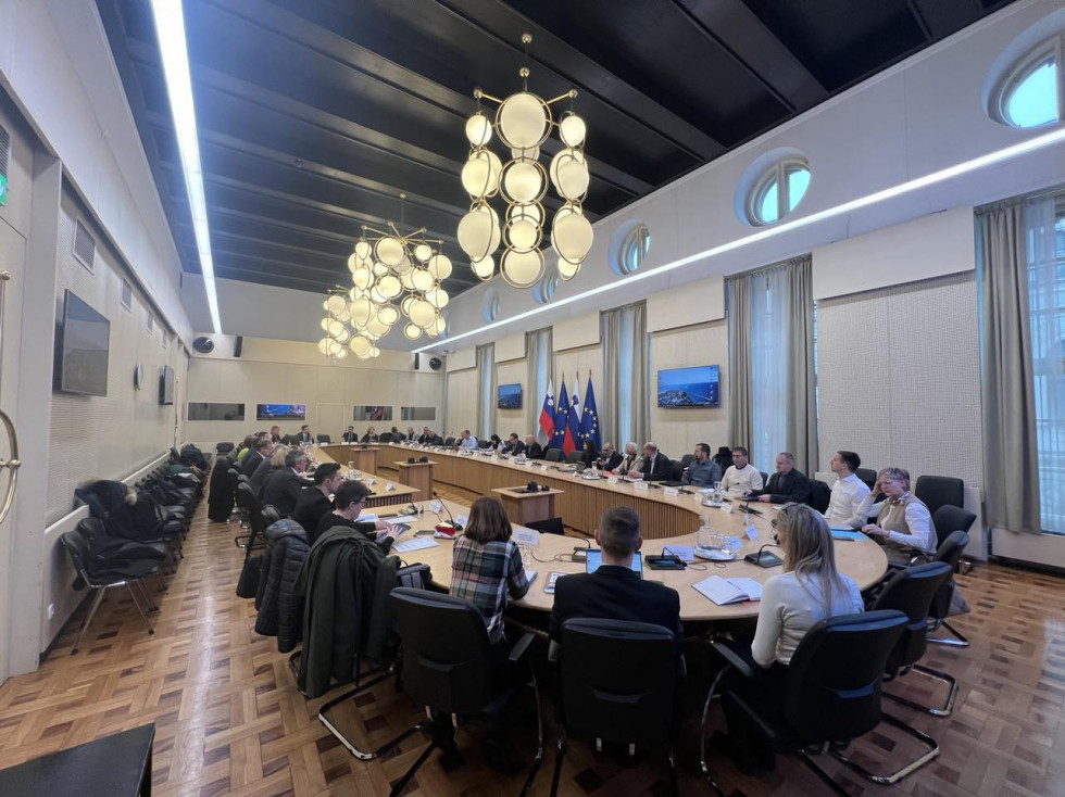Člani inšpekcijskega sveta sedijo v dvorani za veliko, podolgovato, ovalno mizo.