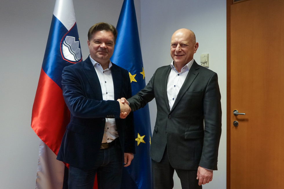 Minister za javno urpavo mag. Franc Props se rokuje z dekanom fakultete za upravo, dr. Mirkom Pecaričem. V ozadju sta Slovenske zastava (desno) in Evropska zastala (levo).
