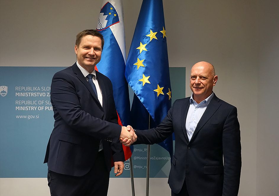 Rokovanje novega direktorja Zorčiča in ministra Propsa. Stojita pred zastavami slovenko in EU zastavo in se rokujeta