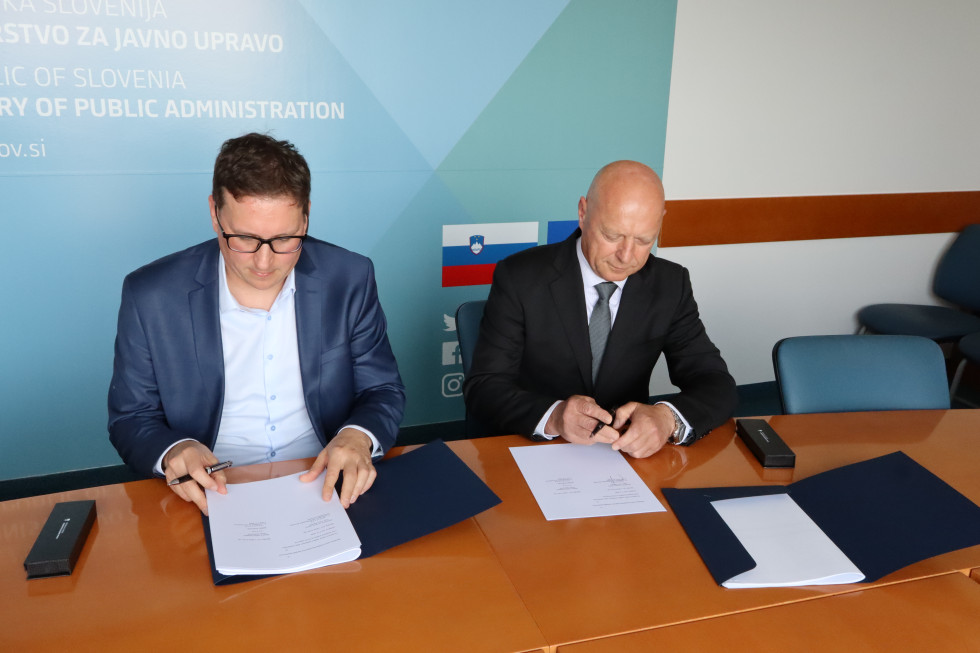 Za mizo sedita moška in podpisujeta vsak svoj dokument.