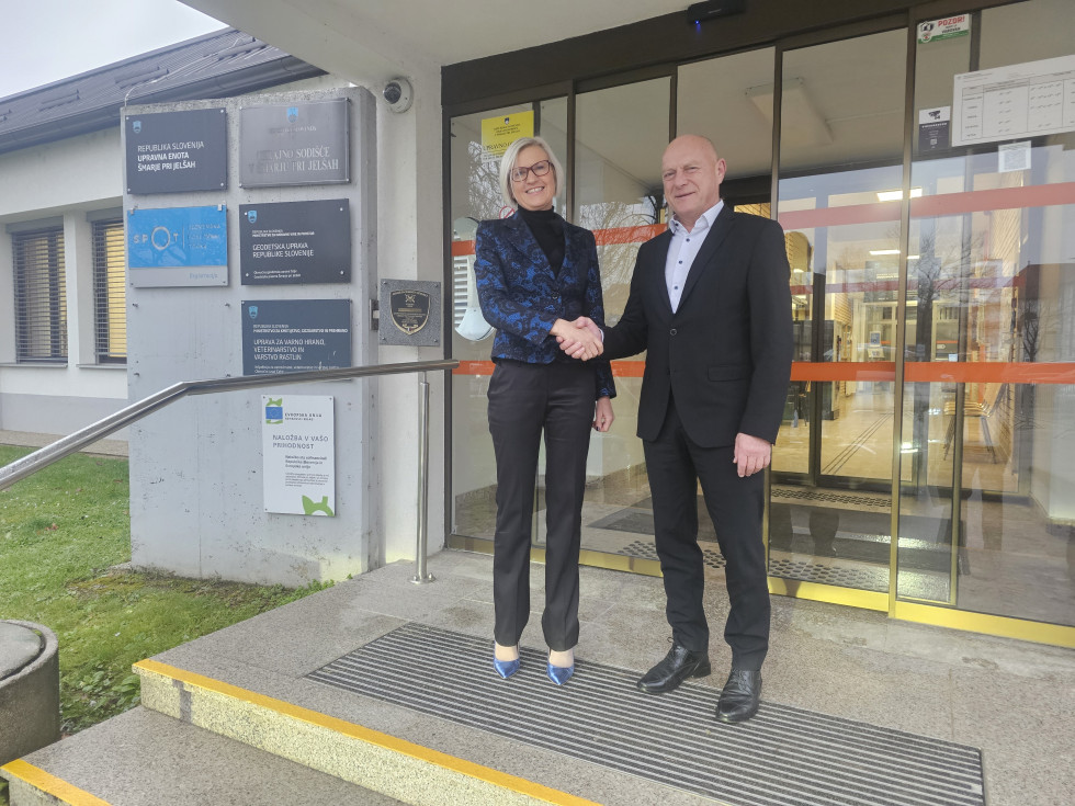 Moški in ženska stojita pred steklenimi vhodnimi vrati in se rokujeta. 