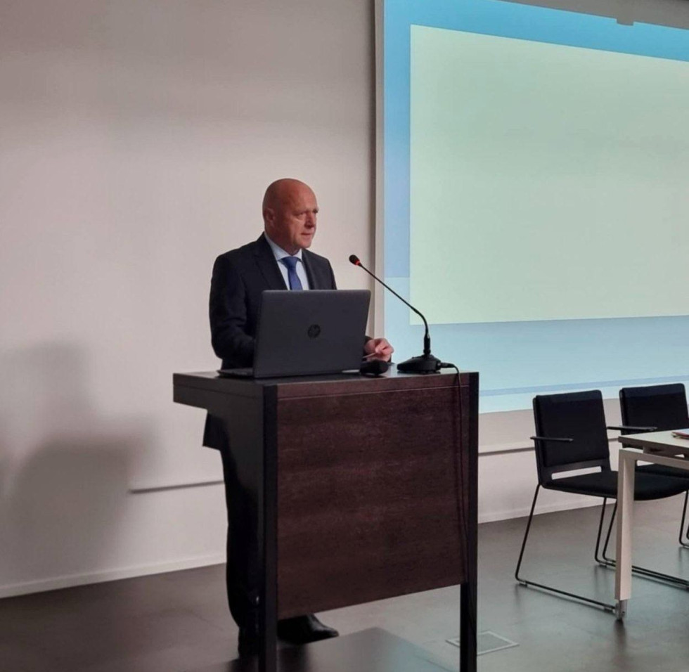 Moški stoji za govorniškim pultom in govori.