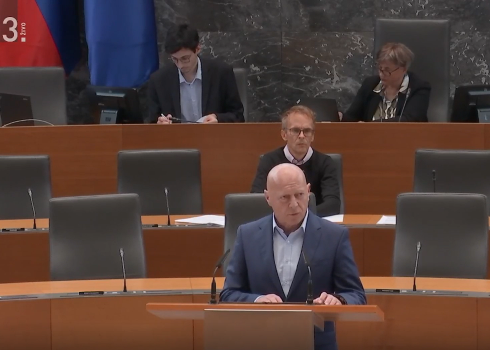 zajem zaslona - minister stoji za govornico v veliki dvorani državnega zbora