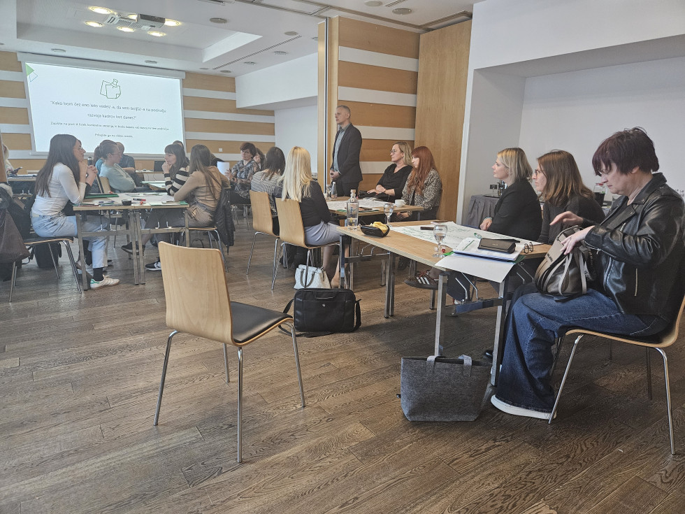 udeleženci usposabljanja sedijo za več manjšimi okroglimi mizami med izvajanjem delavnice