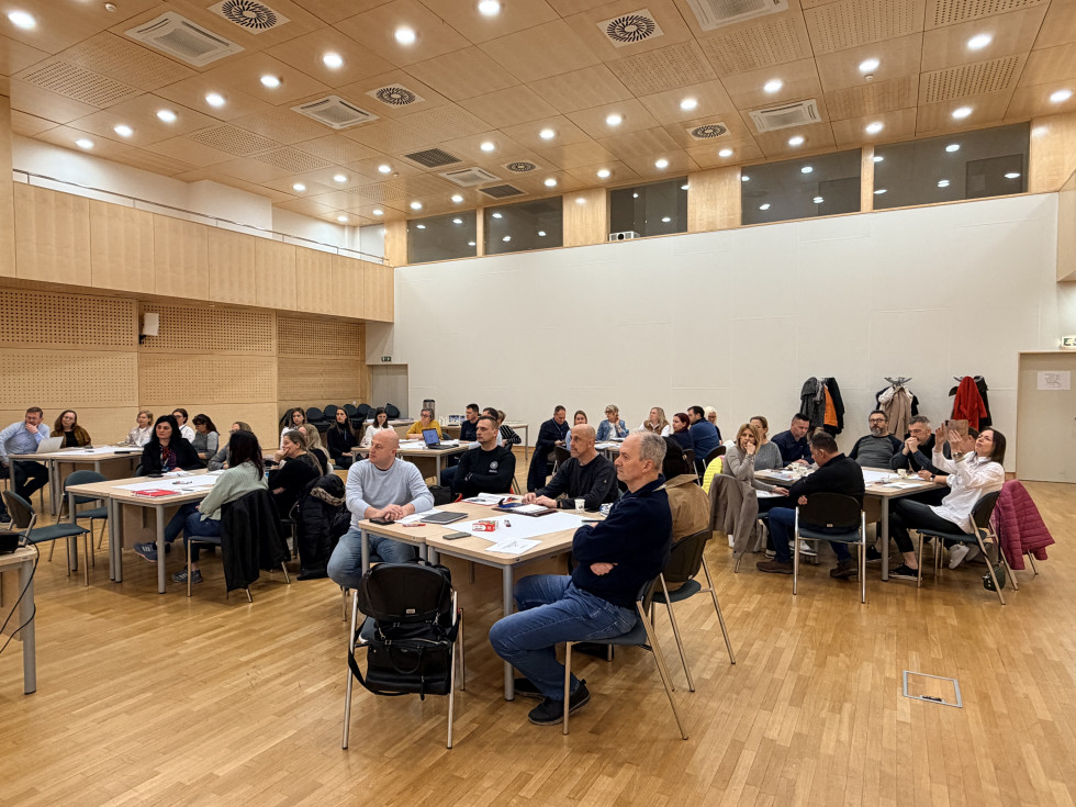 udeleženci sedijo v dvorani za mizami