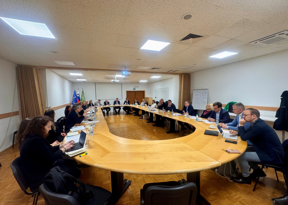 udeleženci srečanja sedijo za ovalno mizo med sestankom