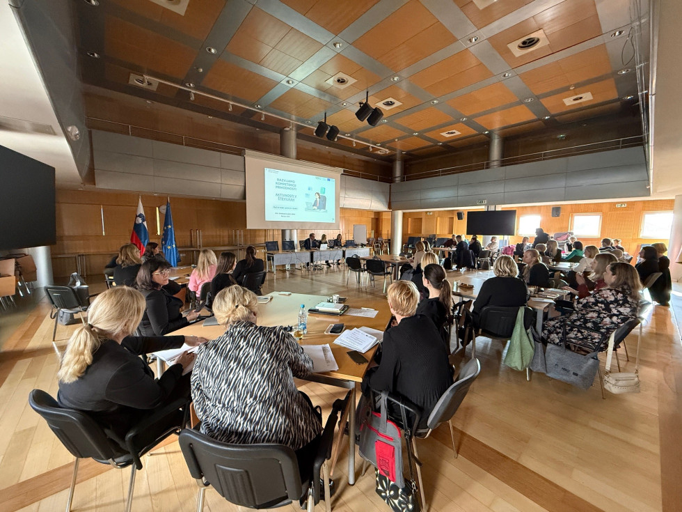 udeleženci predstavitve sedijo v dvorani, razporejeni za mizami v več skupinah