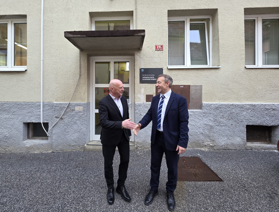 Sprejem ministra pred stavbo upravne enote, kjer si z vodstvom upravne enote podata roke ob prihodu na obisk.