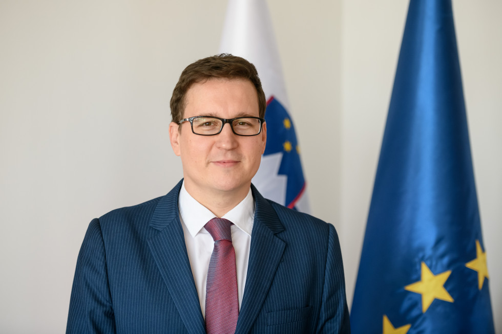 fotografija ministra, v ozadju slovenska in EU zastava