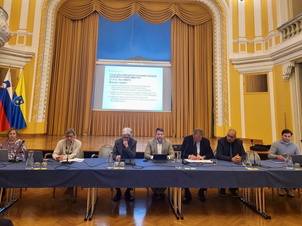 Za glavno mizo sedijo so predstavniki vlade, ministrstev, občin in upravnih enot, v ozadju je projekcija s predstavitvijo rešitev za izdajo gradbenih dovoljenj na podlagi prostorskih aktov.