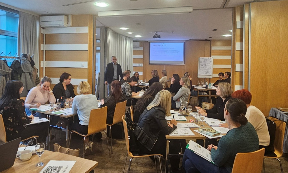 Udeleženci po skupinah sedijo za mizo in sodelujejo pri usposabljanju.