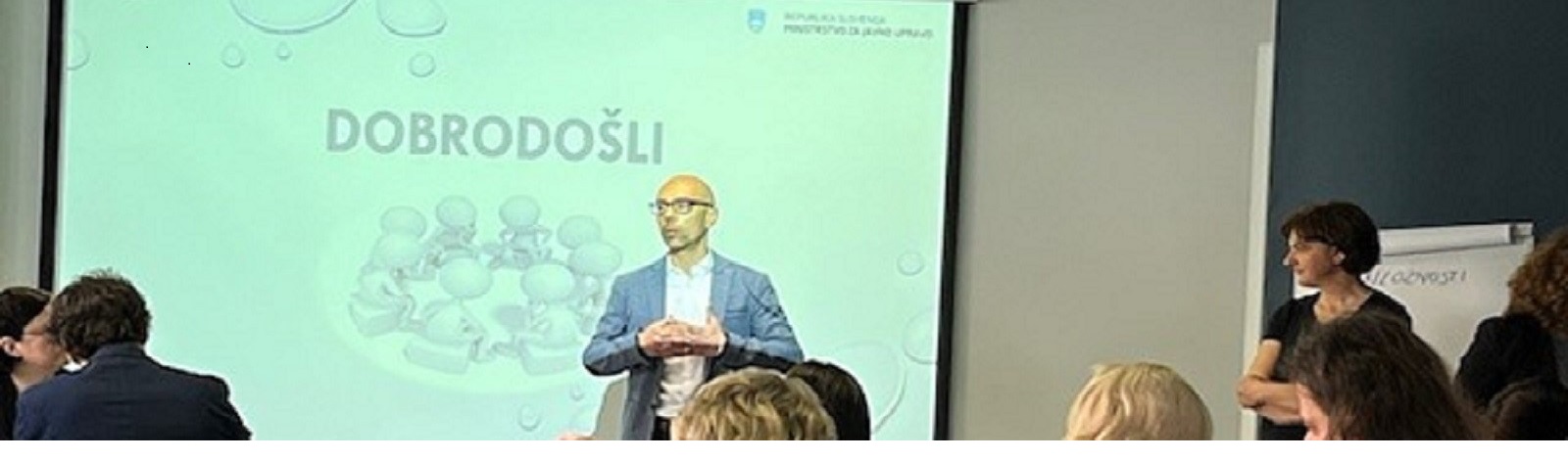 Na sliki je napis z dobrodošlico na delavnici za reševanje izziva za mikrodokazila in vodja projekta dr. Til Rozman, poleg njega je tudi nekaj udeležencev delavnice.