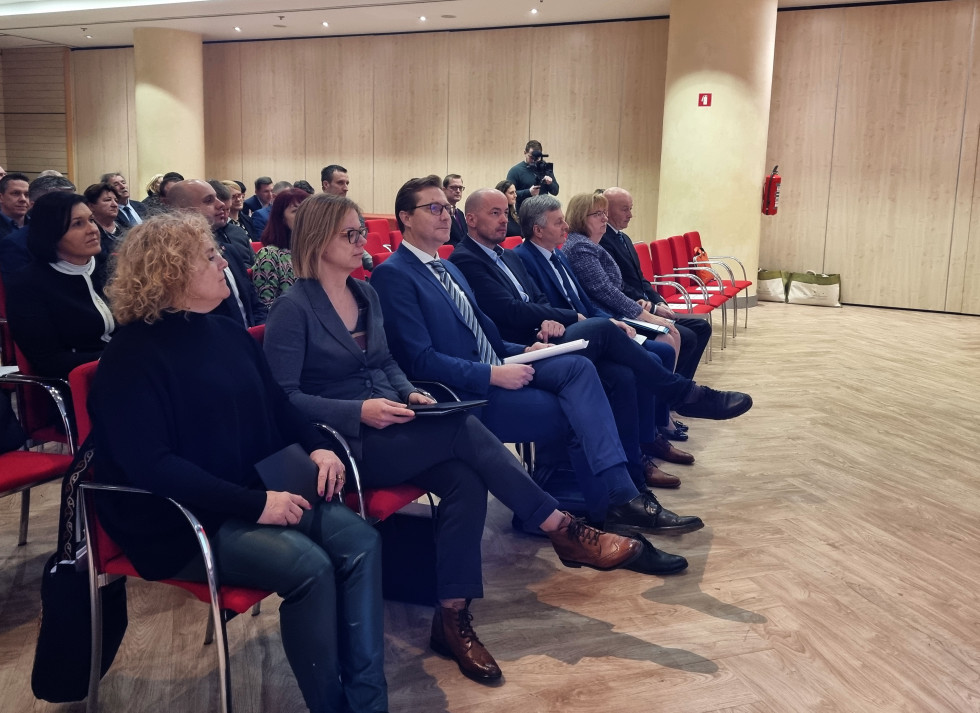 Gostje sedijo v dvorani, v prvi vrsti predsednik Skupnosti občin Slovenije, generalna sekretarka in ministrica Sanja Ajanović Hovnik