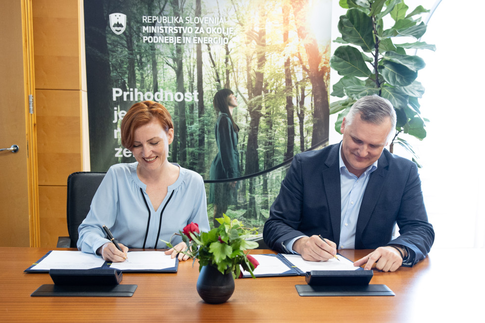 Ministra podpisujeta vsak svoj list papira, ki je pred njima na mizi v modri mapi