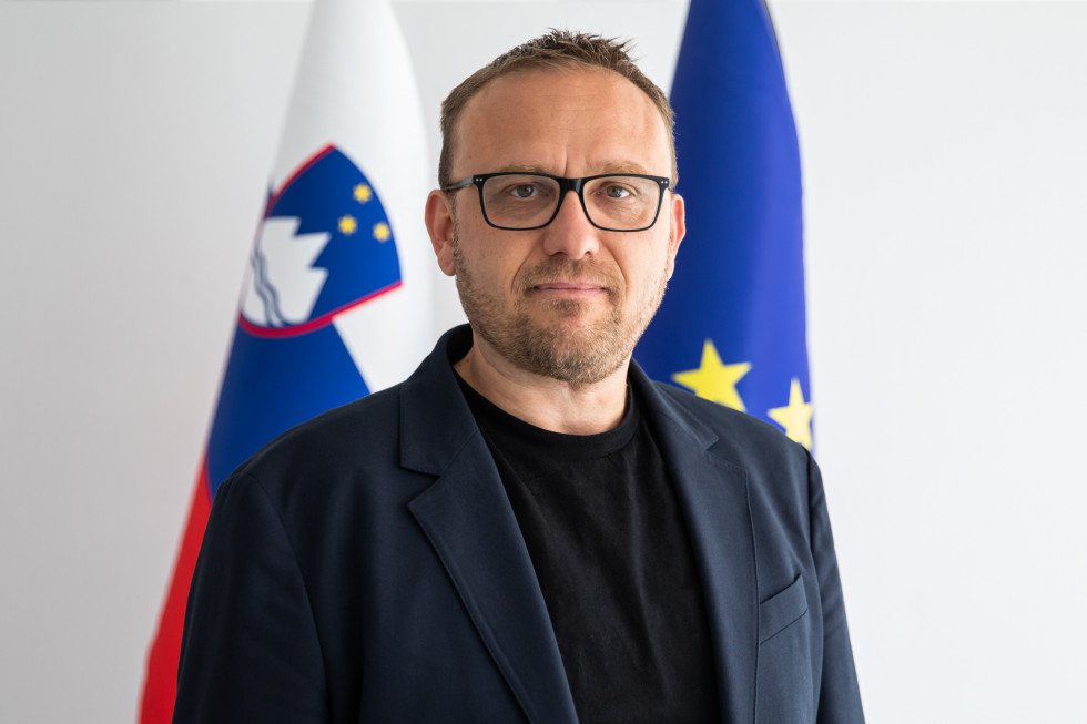 Portrait of a man, in the background the Slovenian flag and the flag of the European Union