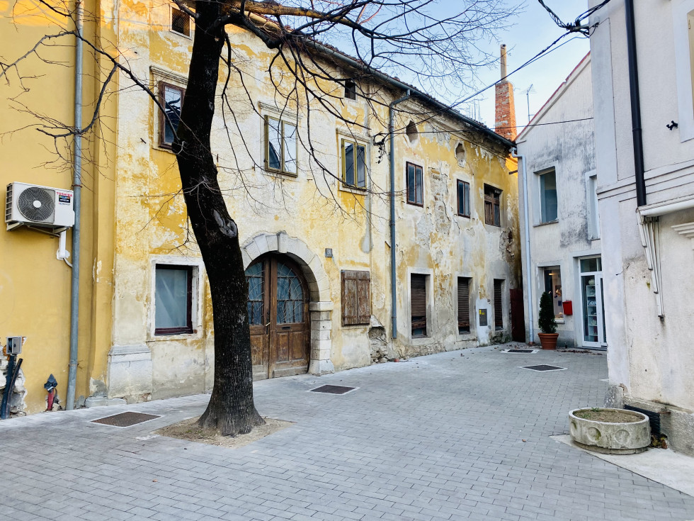 Pogled iz leve strani na prednjo stran propadajoče hiše z rumeno fasado