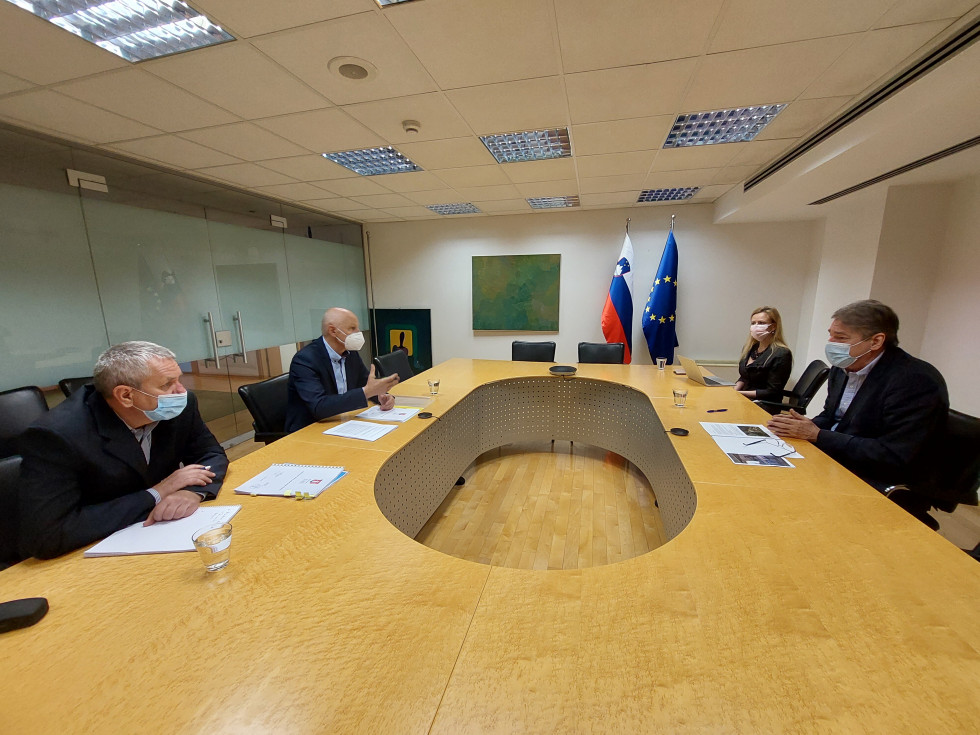 Pogled s strani na štiri osebe, ki med sestankom ministra za kulturo in župana občine Kostel sedijo za isto mizo