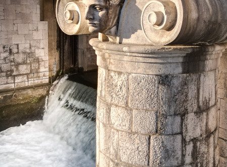 Detajl glave na stebru vodne zapornice na Ljubljanici, ki sledi antični likovni tradiciji in simbolizira slovo reke od samega mestnega središča.