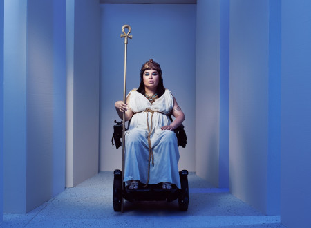 Ženska oblečena v Kleopatro na invalidskem vozičku z zlato palico v levi roki  