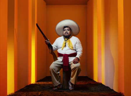 Moški oblečen v mehiškega revolucionarja sedi na solu in v levi roki drži piško